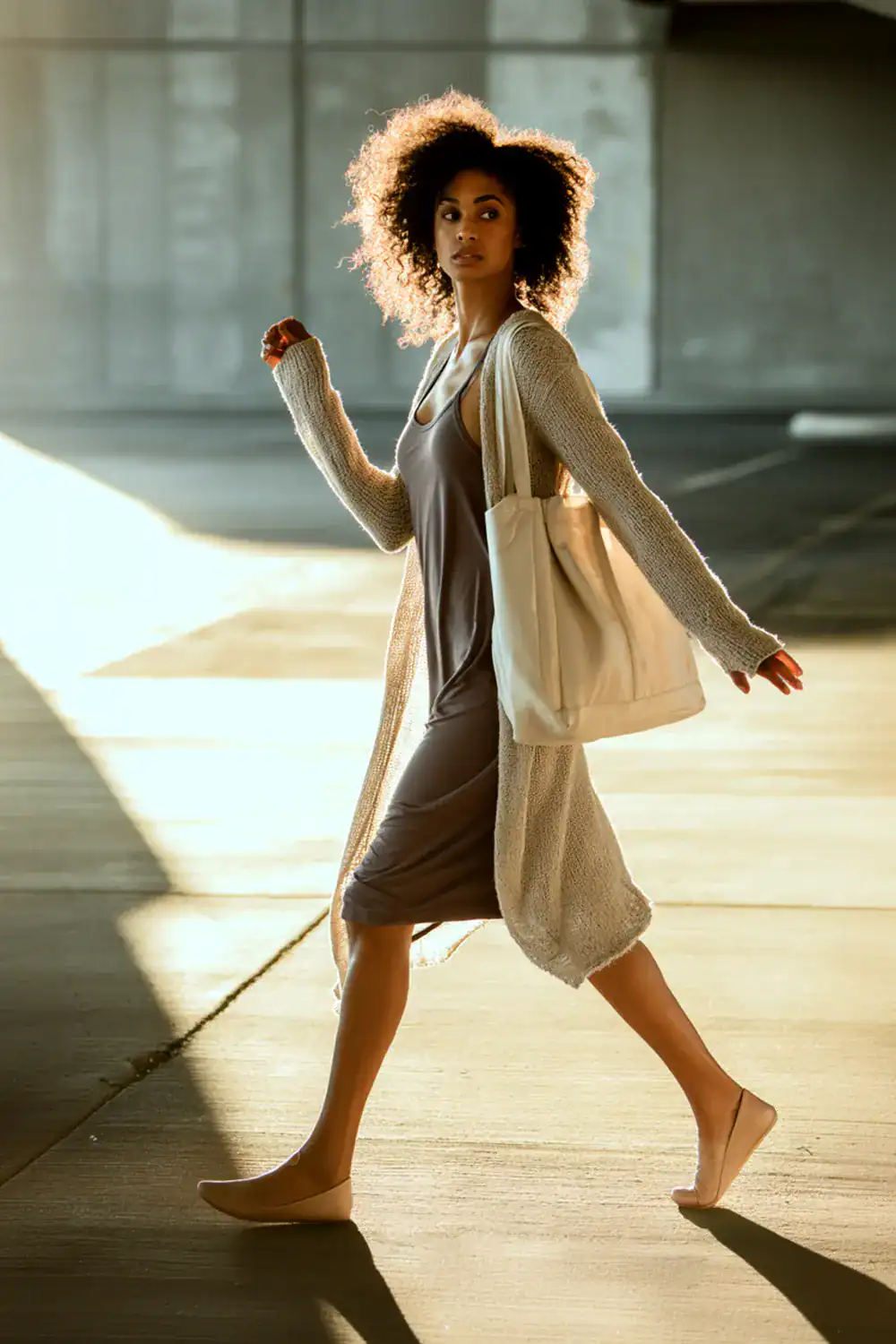 Frau trägt leichtes Strickkleid mit offenem Cardigan und Canvas-Tasche im Sonnenlicht – stilvolles Layering-Outfit für Frühling und Sommer