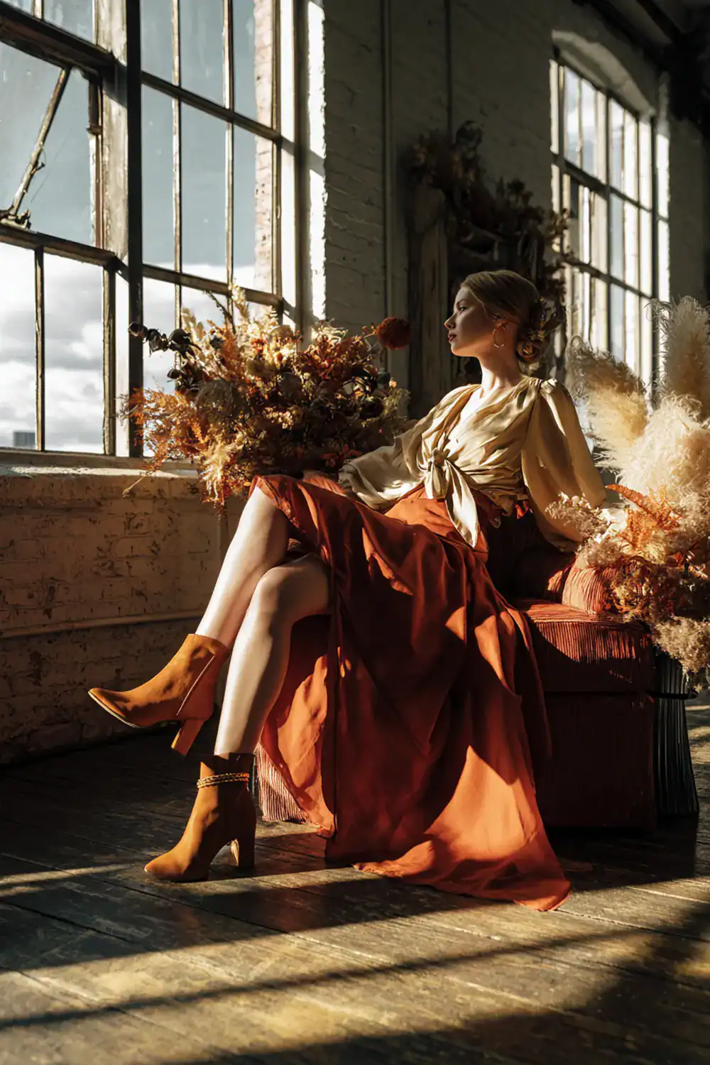 Elegante Frau im Loft mit goldener Bluse, rostfarbenem Rock und Ankle Boots – Herbstmodetrends für Frauen