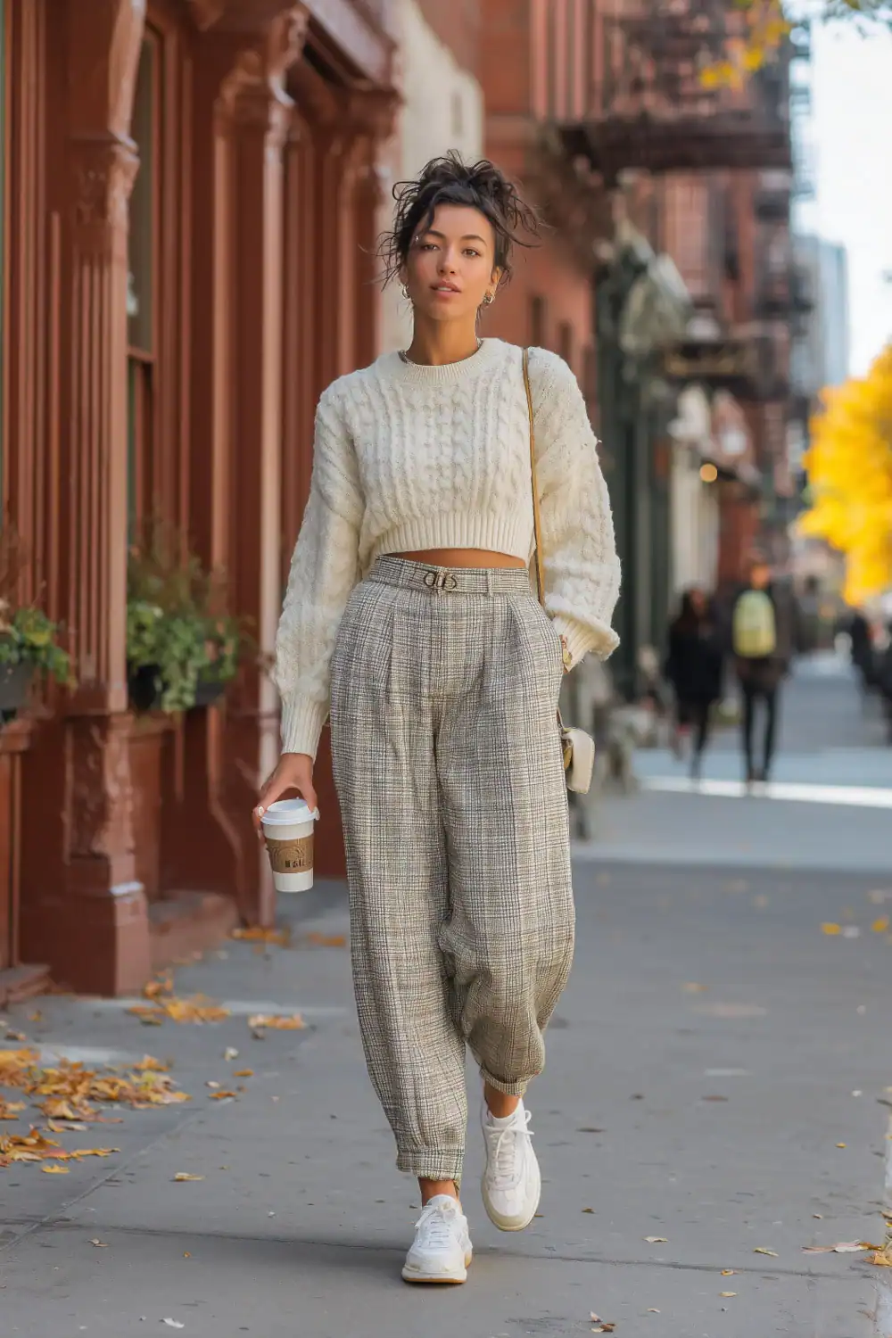 Frau in Karo-Hosen mit cropped Strickpullover und weißen Sneakers auf der Straße, lässiges Herbst-Outfit mit Coffee-to-go